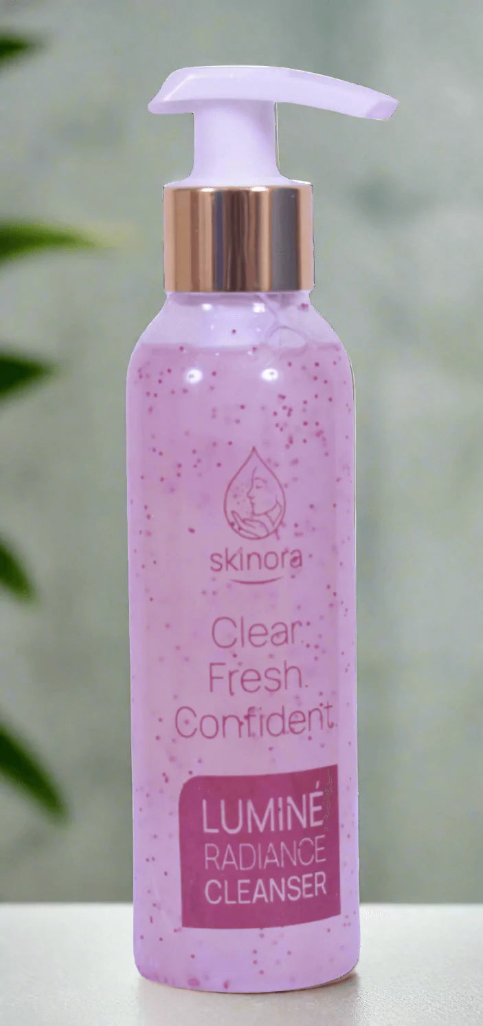 Pink bottle of Lumine Radiance Cleanser with a pump on a blurred green background
